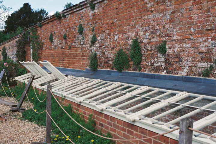 A long greenhouse structure against a brick wall.