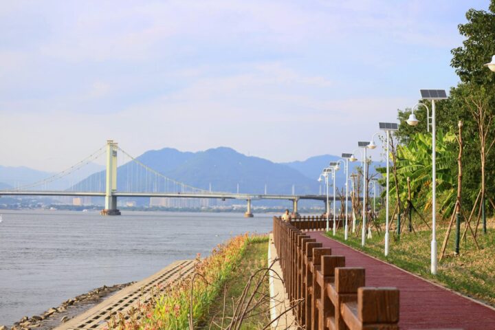 Riverside walkway with bridge and mountains in distance.