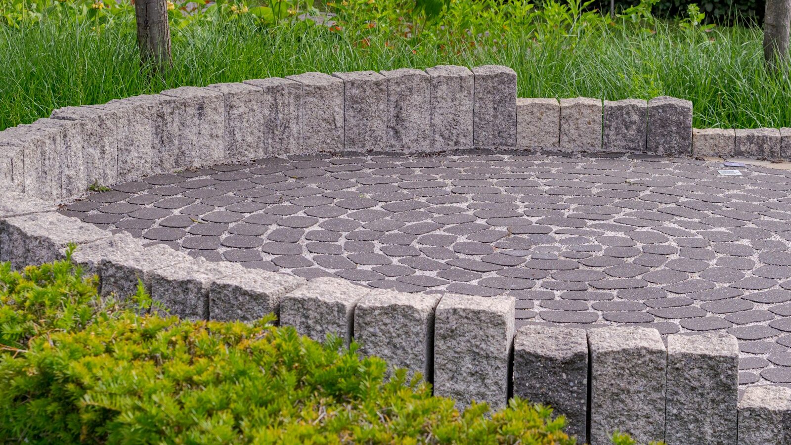 Circular paved patio with low stone wall and green bushes.