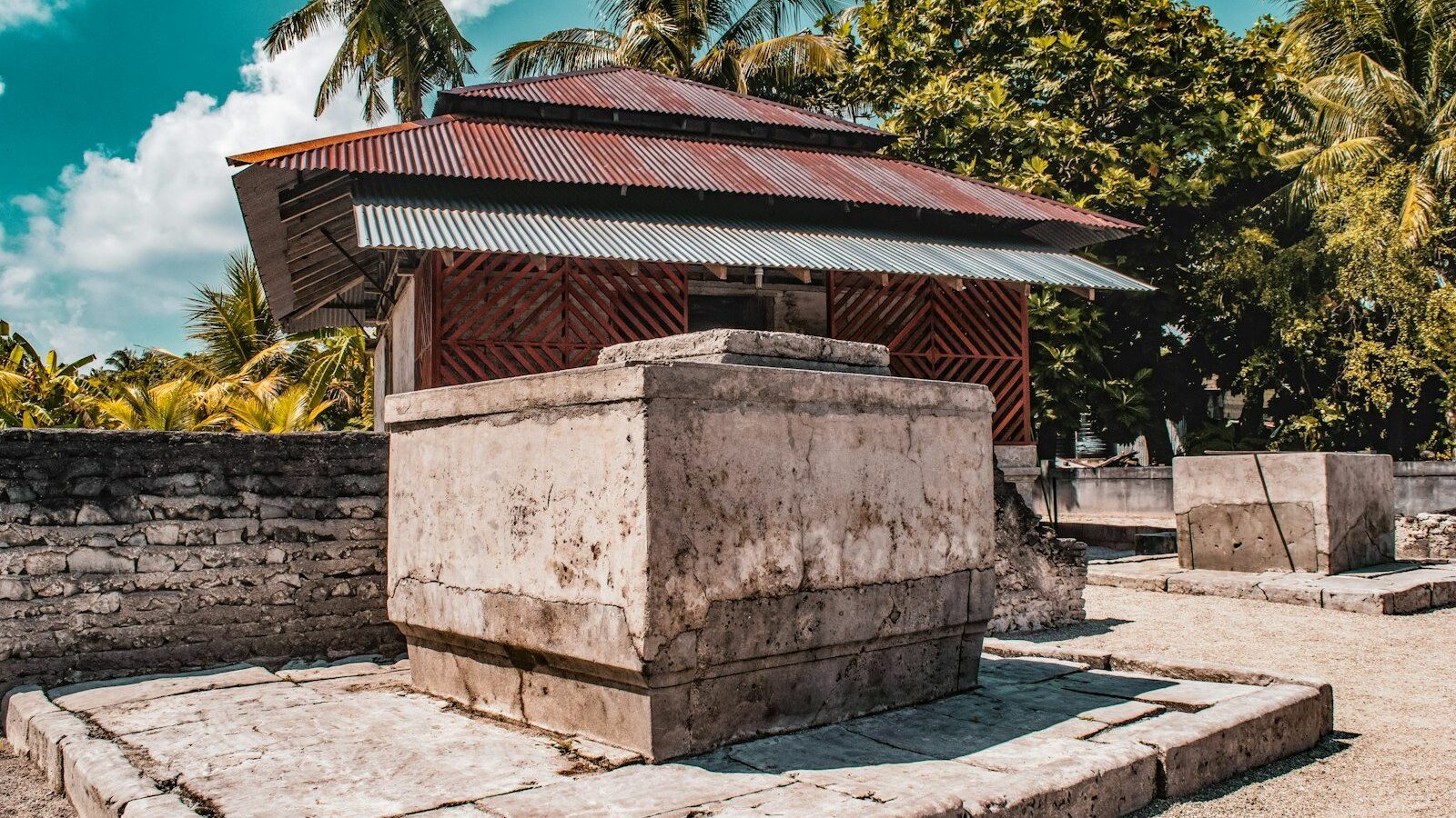 Small stone structure with a metal roof surrounded by trees.