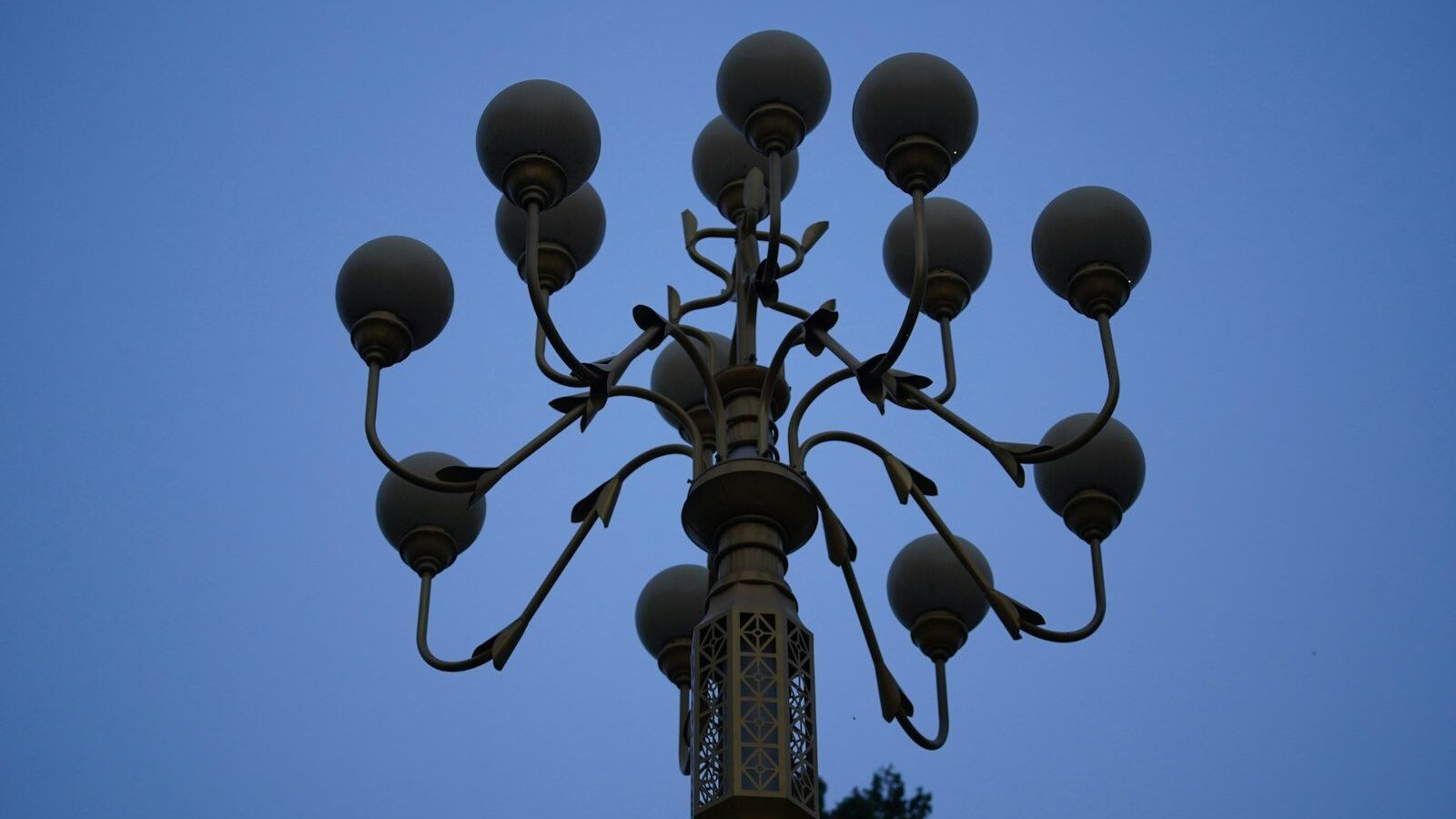A multi-armed street lamp with spherical glass globes against a clear blue sky