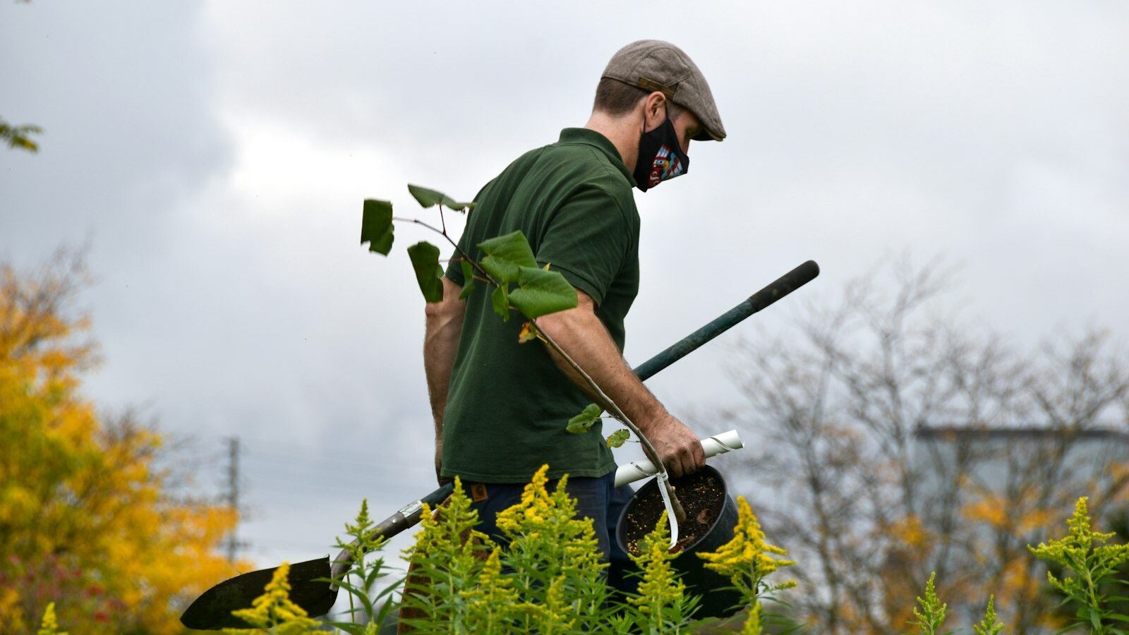 a man in a green shirt holding a pair of gardening tools